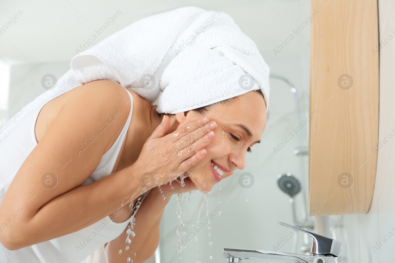 Photo of Happy mature woman washing face in bathroom