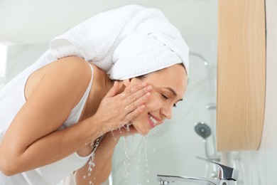 Photo of Happy mature woman washing face in bathroom