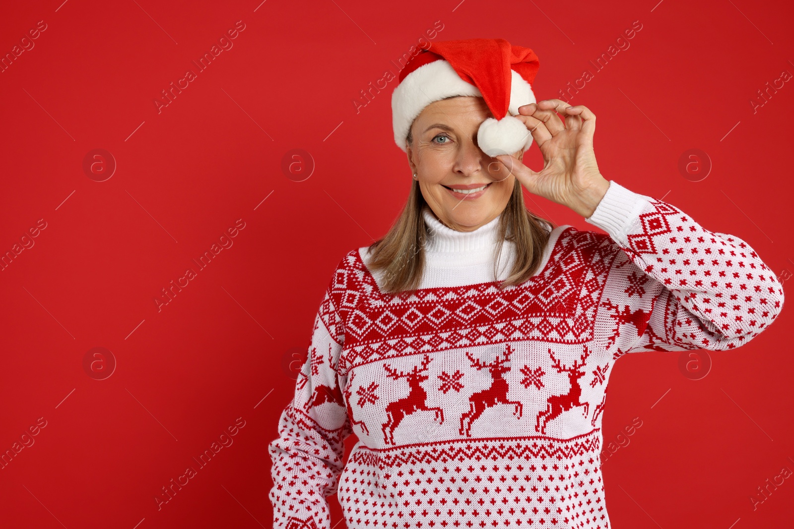 Photo of Happy senior woman in Christmas sweater and Santa hat on red background. Space for text