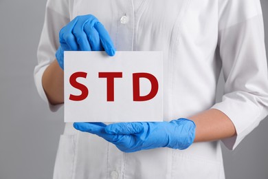 Photo of Doctor holding sheet of paper with abbreviation STD on grey background, closeup
