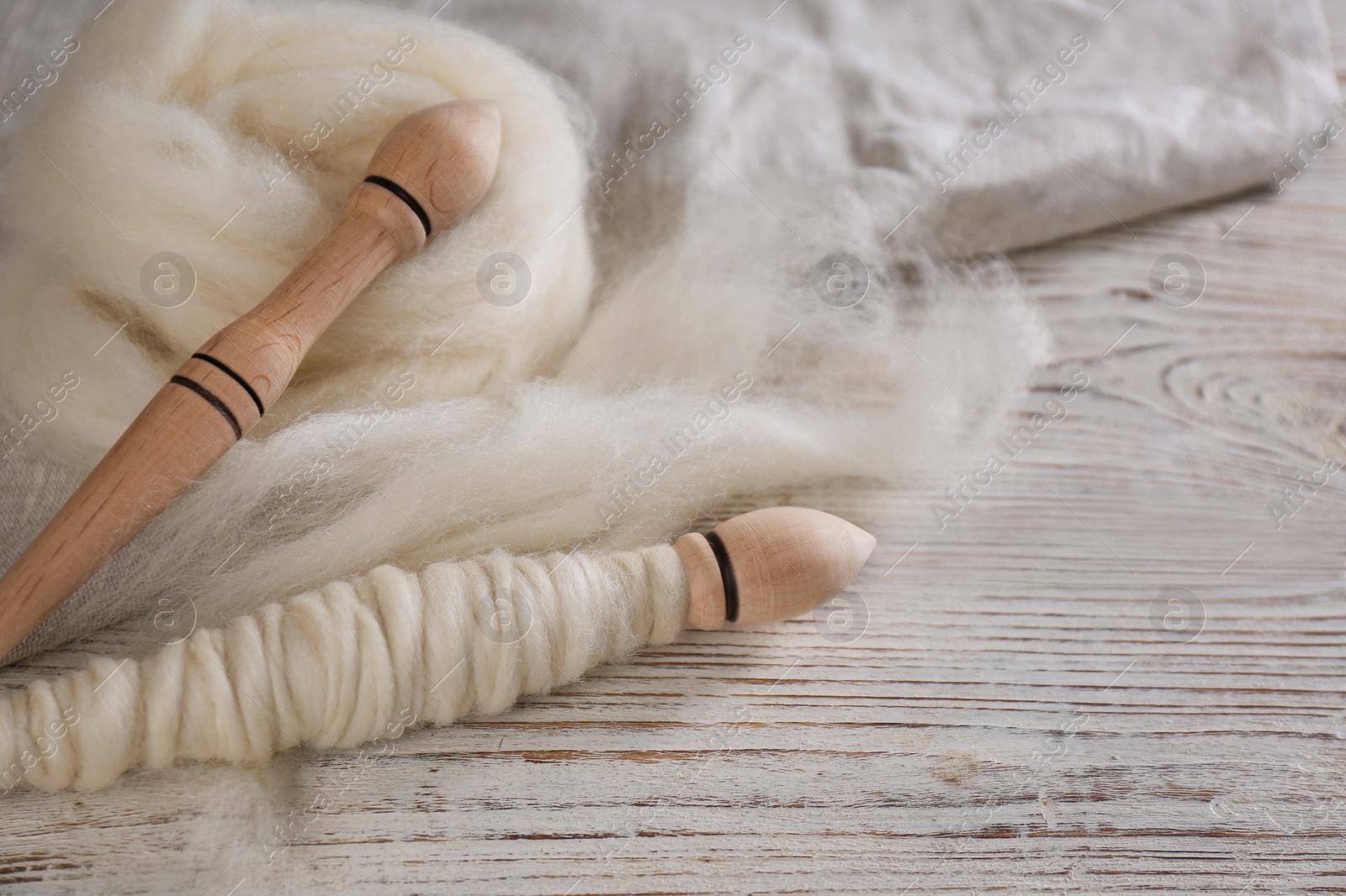 Photo of Soft wool and spindles on white wooden table, closeup