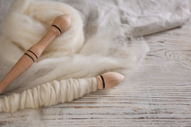 Photo of Soft wool and spindles on white wooden table, closeup