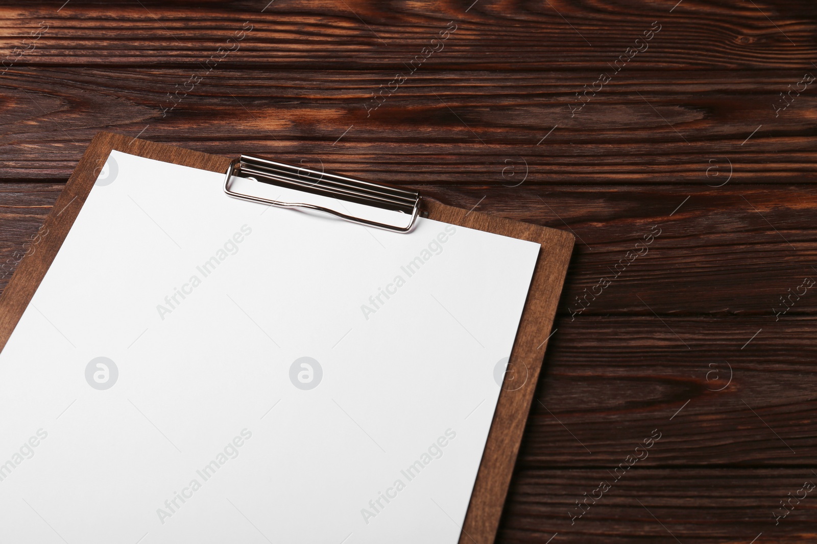Photo of New clipboard with sheet of blank paper on wooden table, above view. Space for text