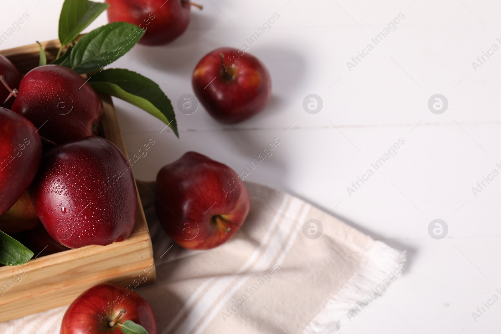 Photo of Fresh red apples with leaves in crate on white wooden table. Space for text