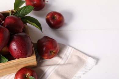 Photo of Fresh red apples with leaves in crate on white wooden table. Space for text