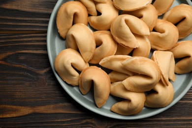 Tasty fortune cookies with predictions in plate on wooden table, top view