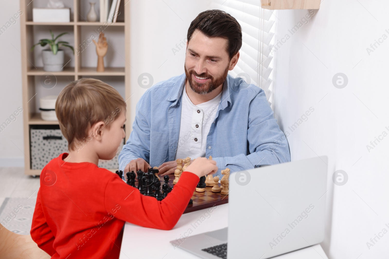 Photo of Father and son playing chess following online lesson in room