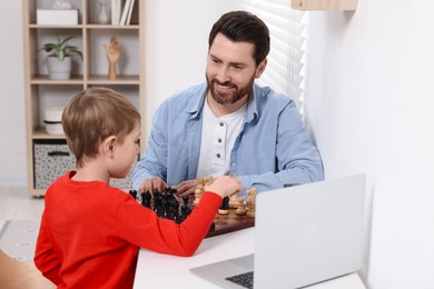 Father and son playing chess following online lesson in room