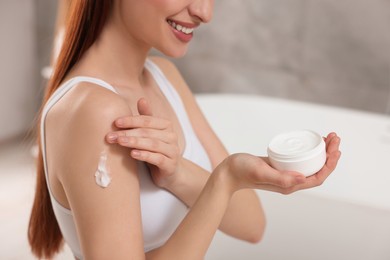 Young woman applying body cream onto shoulder in bathroom, closeup