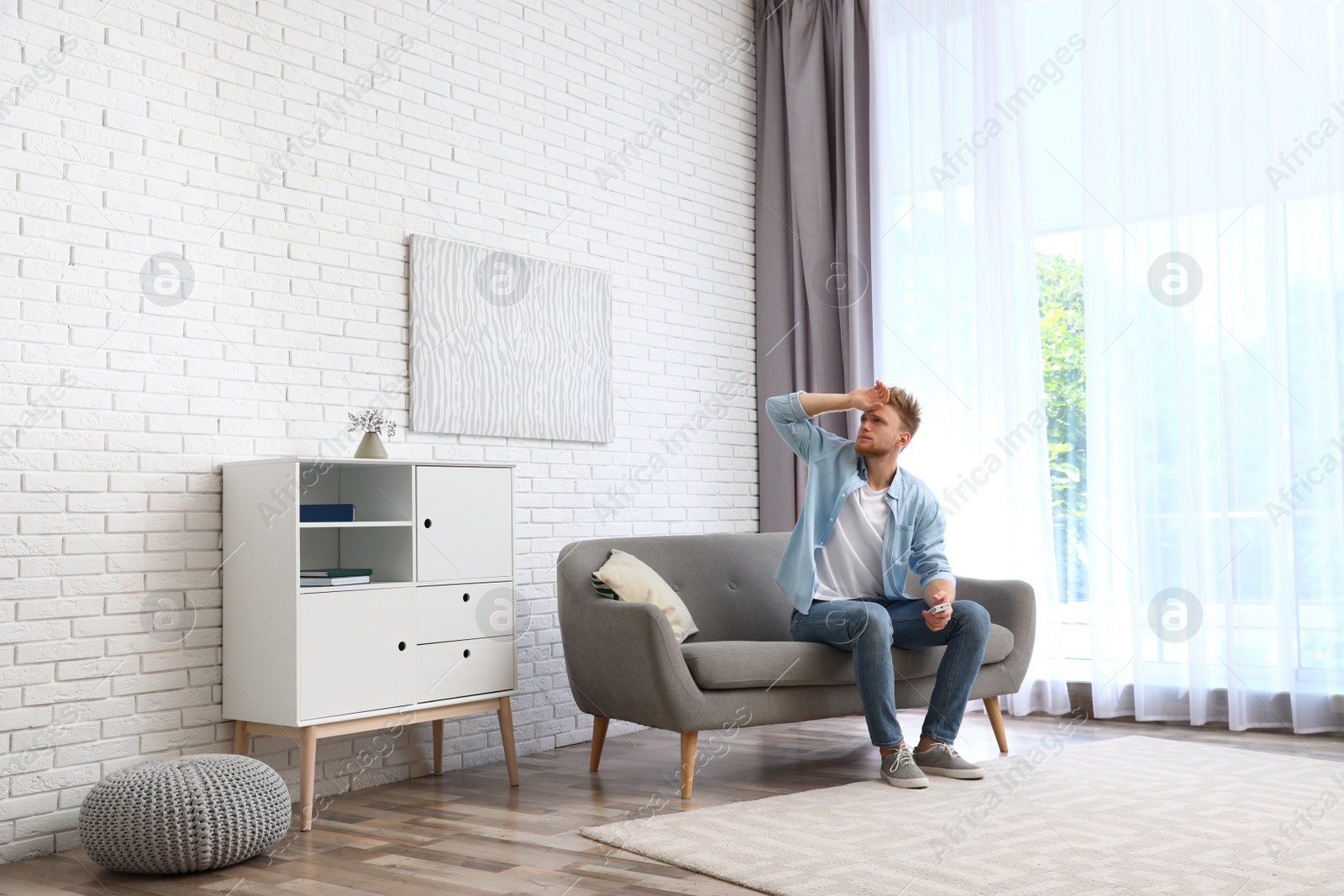 Photo of Young man suffering from heat under broken air conditioner at home