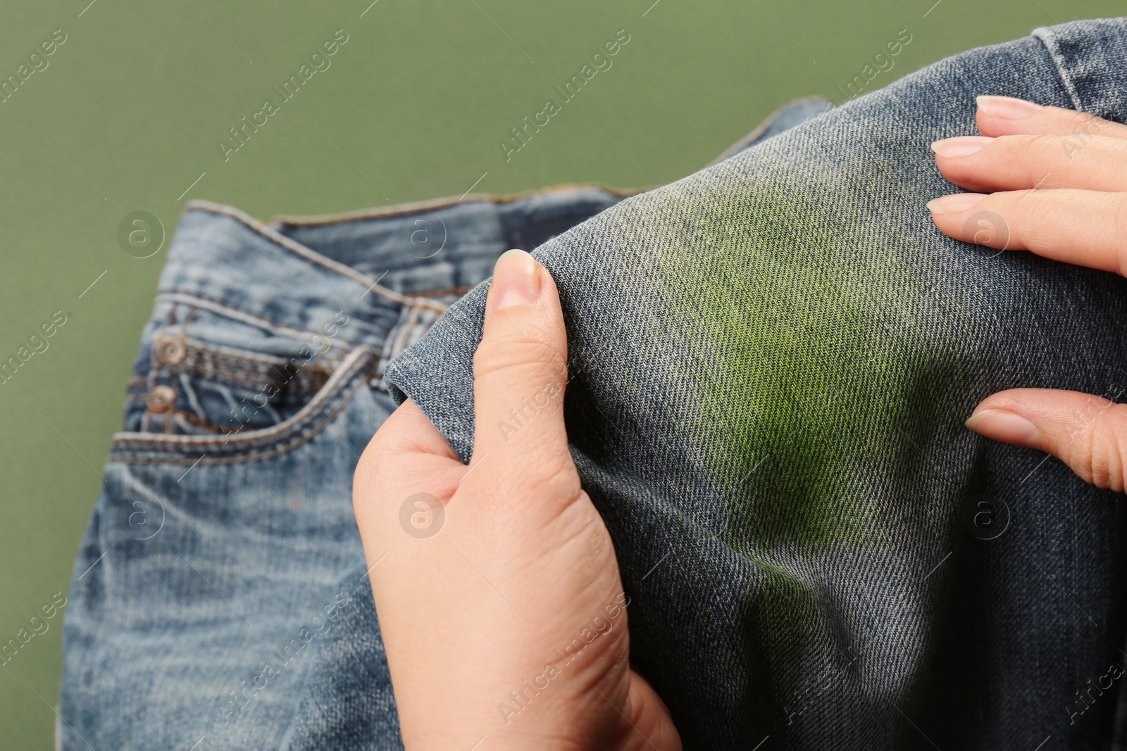 Photo of Woman holding jeans with stain on green background, closeup