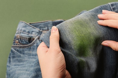 Photo of Woman holding jeans with stain on green background, closeup