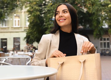 Photo of Young woman with stylish bag at table in outdoor cafe