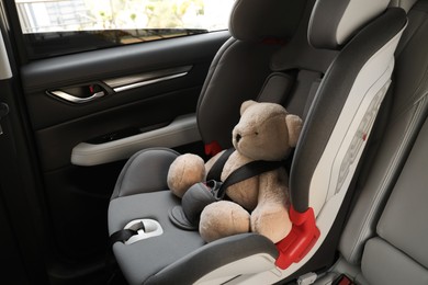 Teddy bear fastened with car safety belt in child seat