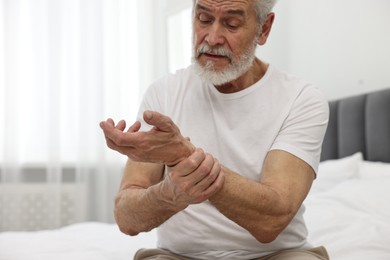 Arthritis symptoms. Man suffering from pain in wrist on bed at home