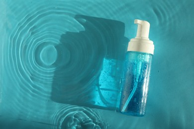 Photo of Bottle of cosmetic product in water on turquoise background, top view. Space for text
