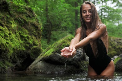 Photo of Beautiful young woman splashing water in mountain river outdoors. Space for text