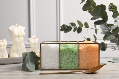 Different types of sea salt, spoon, candles and eucalyptus branches on wooden table