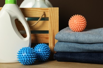 Many dryer balls, stacked clean clothes and laundry detergents on wooden table