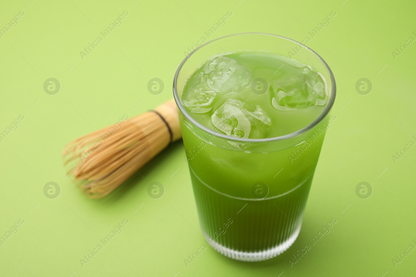 Photo of Glass of delicious iced matcha tea and bamboo whisk on green background, closeup. Space for text