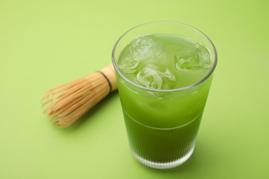 Glass of delicious iced matcha tea and bamboo whisk on green background, closeup. Space for text