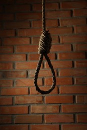 Rope noose with knot hanging near brick wall