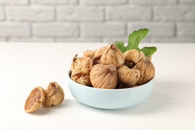 Photo of Bowl with tasty dried figs and green leaf on white wooden table