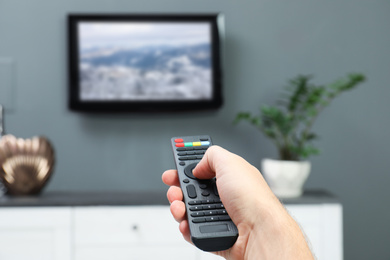 Image of Man switching channels on TV with remote control at home