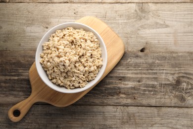 Photo of Tasty boiled oatmeal in bowl on wooden table, top view. Space for text