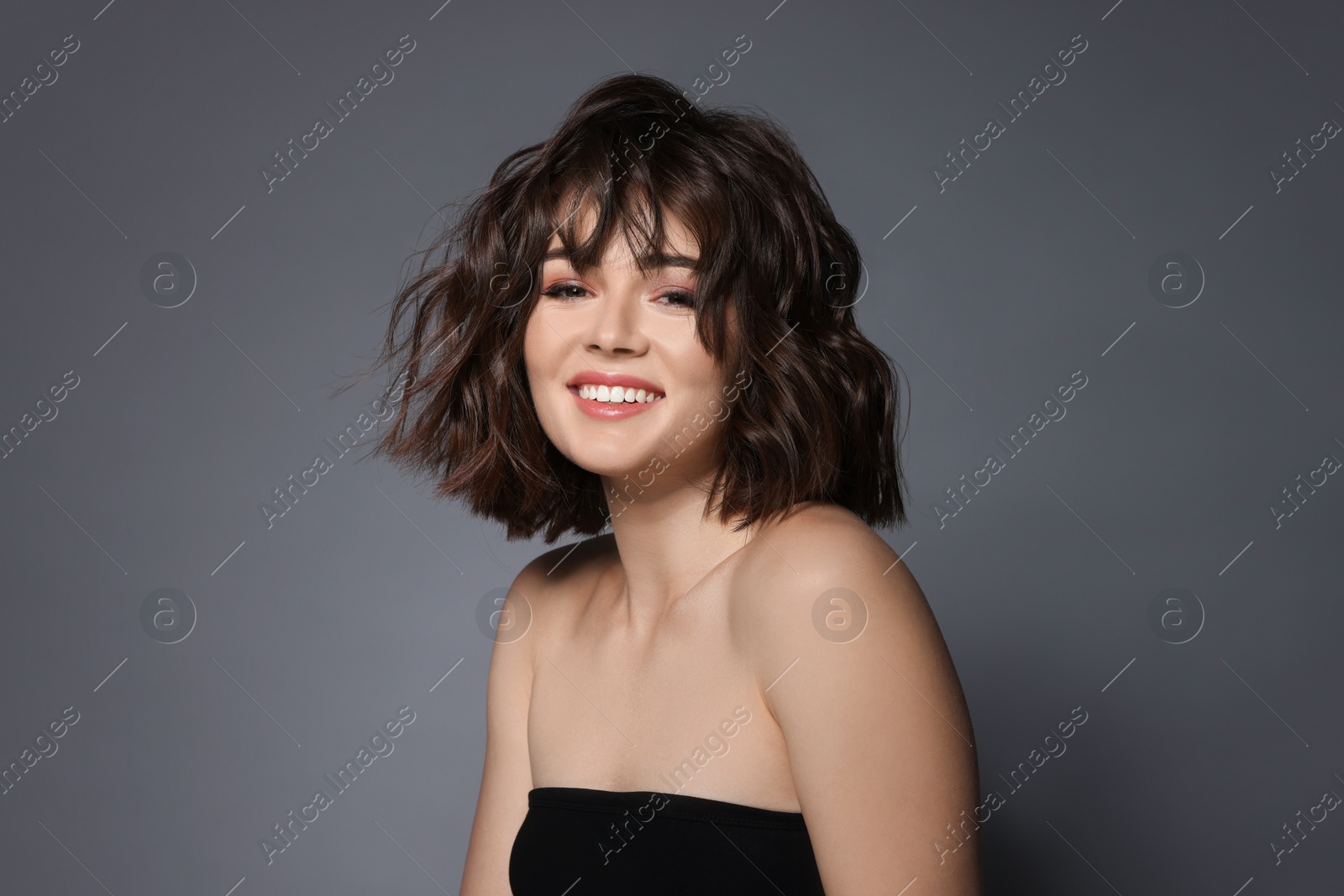 Photo of Portrait of beautiful young woman with wavy hairstyle on grey background