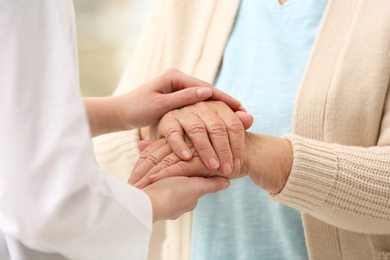 Photo of Nurse comforting elderly woman against blurred background, closeup. Assisting senior generation