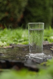 Photo of Glass of fresh water on wooden stump in green grass outdoors. Space for text