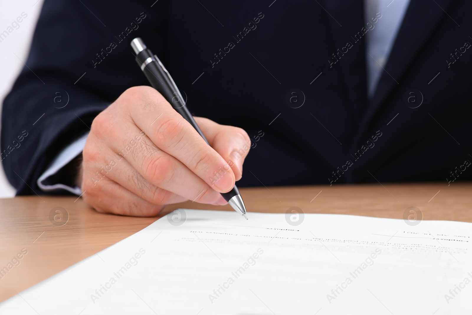 Photo of Businessman signing contract at wooden table, closeup of hand