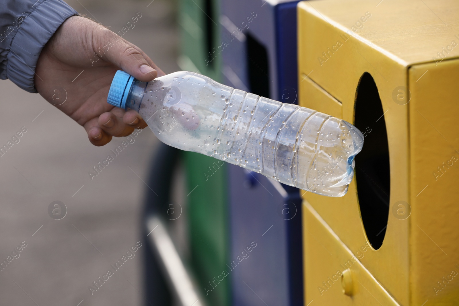 Photo of Man throwing plastic bottle into garbage bin outdoors, closeup. Waste sorting