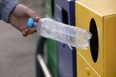 Photo of Man throwing plastic bottle into garbage bin outdoors, closeup. Waste sorting