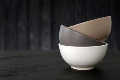 Photo of Stylish empty ceramic bowls on black table, space for text. Cooking utensils