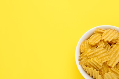 Bowl of tasty ridged potato chips on yellow background, top view. Space for text