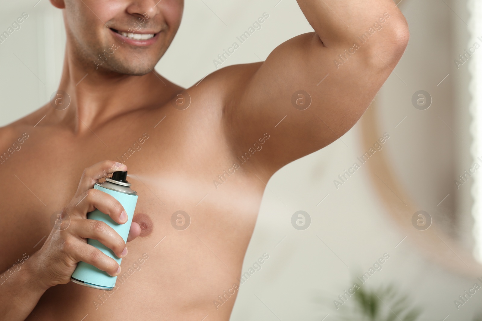 Photo of Young man applying spray deodorant indoors, closeup