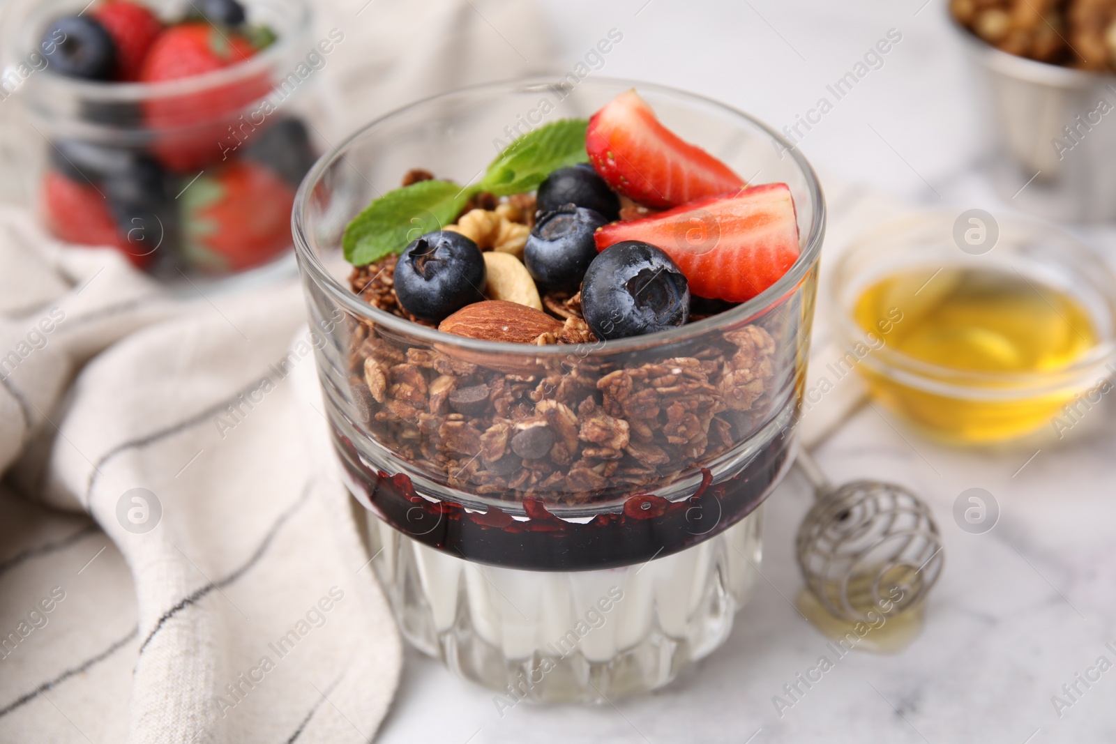 Photo of Tasty granola with berries, nuts, jam and yogurt in glass on white marble table, closeup