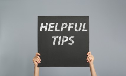 Image of Woman holding poster with phrase Helpful Tips on grey background, closeup