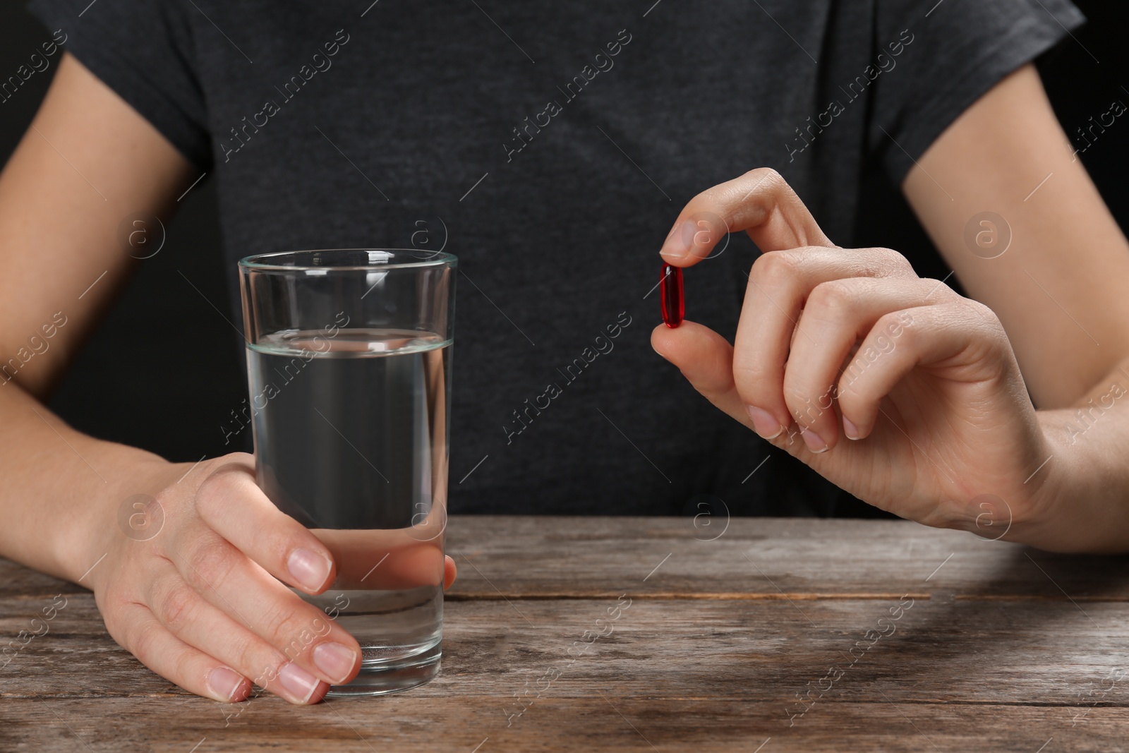 Photo of Woman holding pill and glass of water at table, closeup