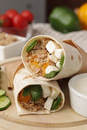 Photo of Delicious tortilla wraps with tuna and vegetables on wooden board, closeup