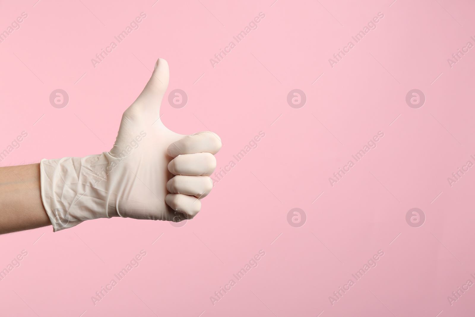 Photo of Person in medical gloves showing thumb up on pink background, closeup of hand. Space for text