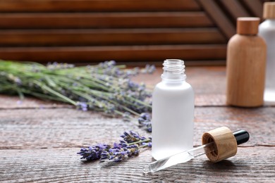 Photo of Bottle of lavender essential oil with flowers on wooden table, space for text