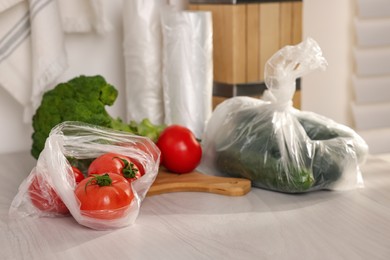 Photo of Plastic bags and fresh vegetables on white table