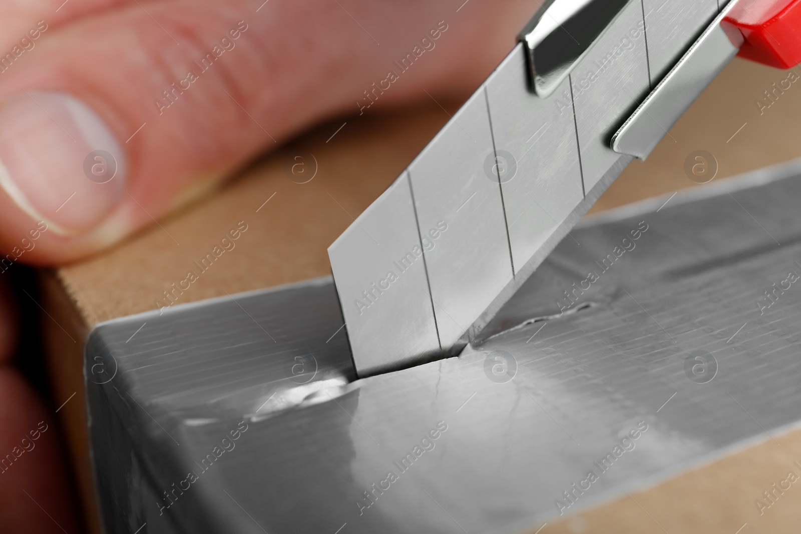 Photo of Man using utility knife to open parcel, closeup