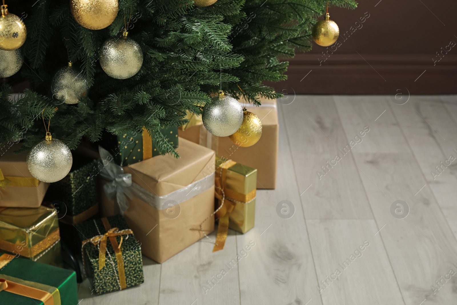Photo of Beautifully decorated Christmas tree and many gift boxes near brown wall indoors, closeup. Space for text