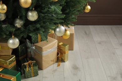Photo of Beautifully decorated Christmas tree and many gift boxes near brown wall indoors, closeup. Space for text