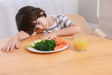 Cute little boy refusing to eat vegetables at home