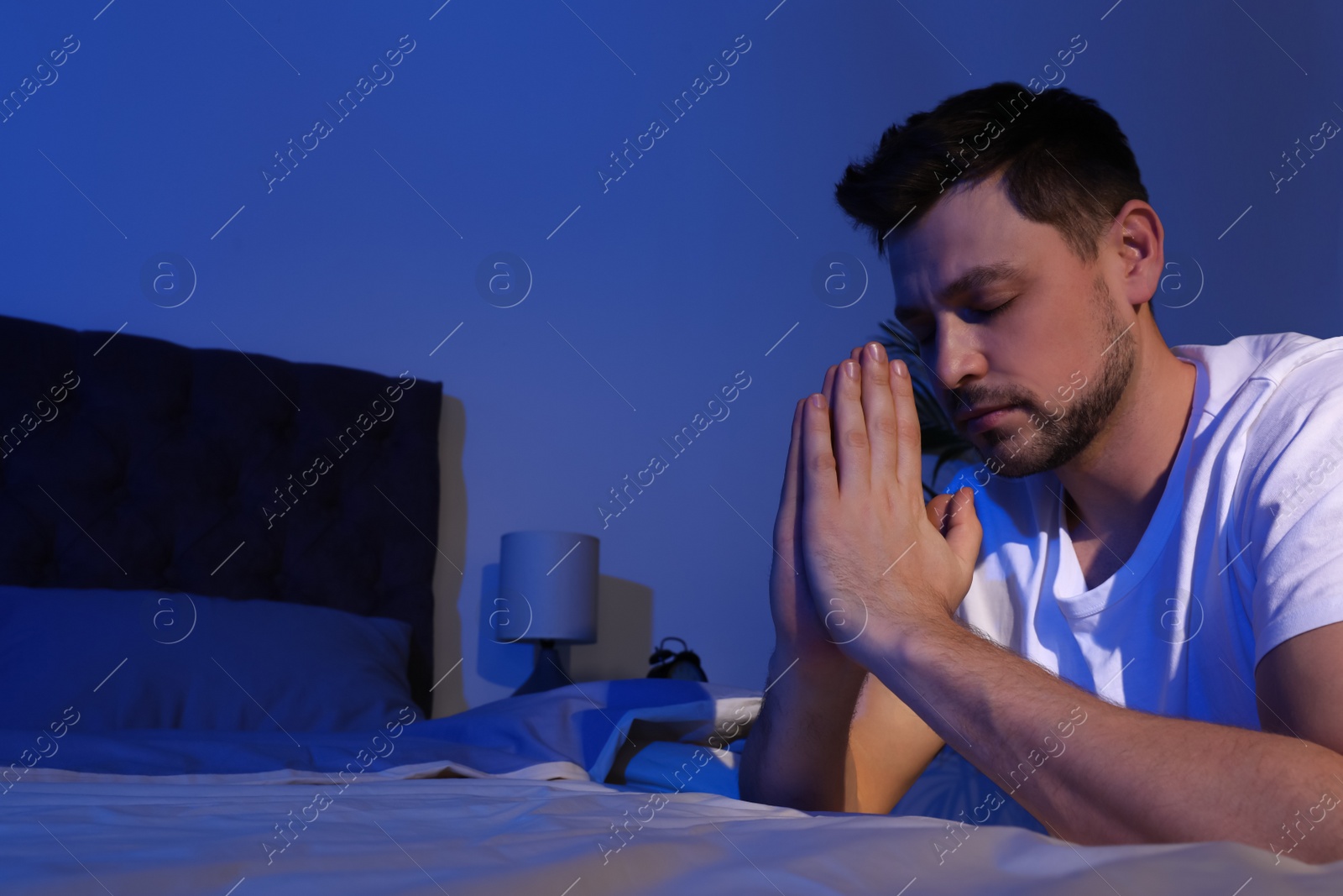 Photo of Handsome man saying bedtime prayer in dark room at night. Space for text